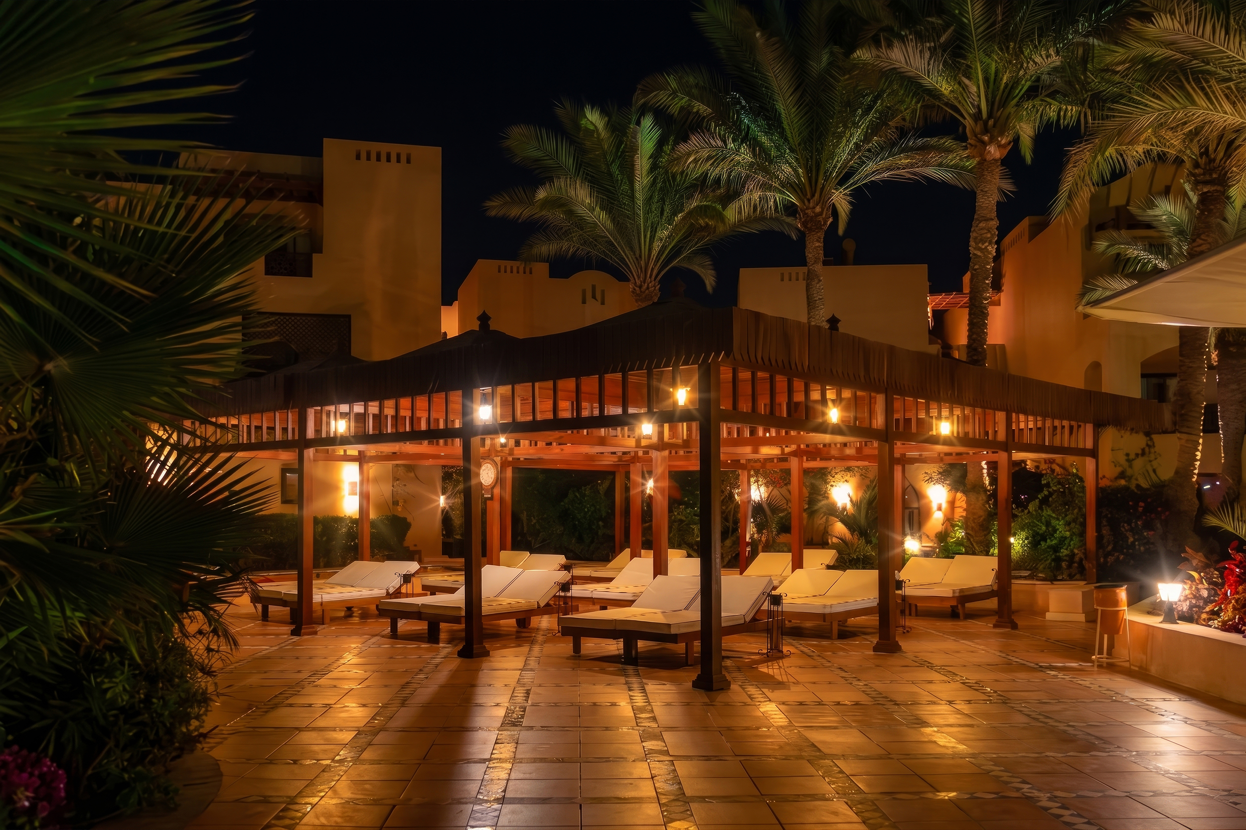 Warmly illuminated wooden pavilion with lounge chairs at night, surrounded by palm trees at Steigenberger Coraya Beach luxury resort.